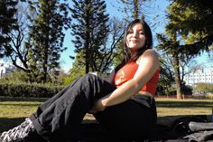 a woman sitting on the ground with her arms crossed and legs crossed, in front of trees