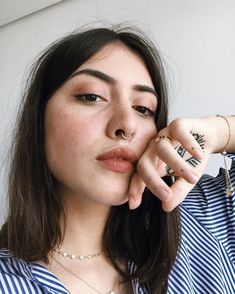 a woman holding her nose with both hands and looking off to the side while wearing a striped shirt