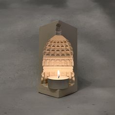 a lit candle in front of a cut out of a building with a dome on top