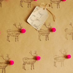 the wrapping paper has pink pom - poms on it and is decorated with deer silhouettes