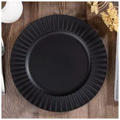 a black paper plate sitting on top of a wooden table next to a fork and knife