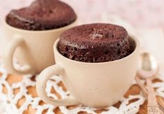 two cupcakes sitting in mugs on a doily next to each other