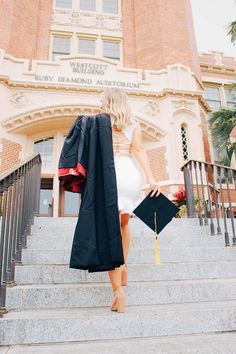 a woman is walking down the stairs with her graduation gown and book in front of an old building