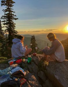 two people sitting on the edge of a cliff at sunset eating food and drinking water