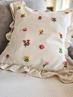 a close up of a pillow on a couch with flowers and ruffles embroidered on it