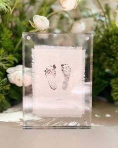 a clear box with a baby's footprints on it and flowers in the background