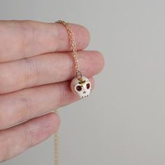 a person holding a tiny skull necklace in their left hand and wearing a gold chain