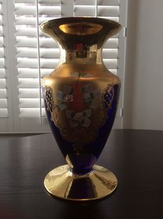 a blue and gold vase sitting on top of a wooden table next to a window