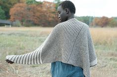 a person standing in a field with a sweater over their shoulders and hands out to the side