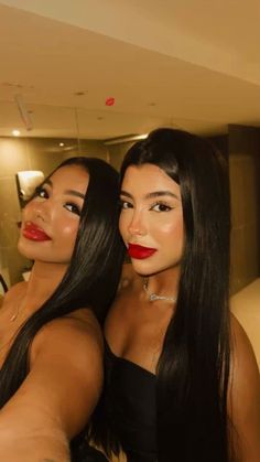 two women with long black hair and red lipstick posing for the camera in front of a mirror