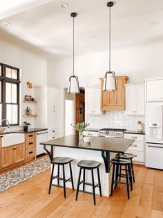 a large kitchen with wooden floors and white walls, has an island table surrounded by stools