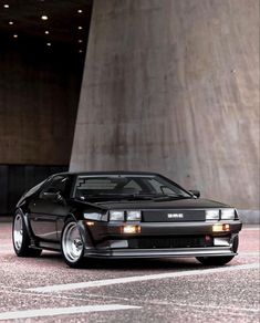 a black sports car parked in front of a tall concrete building with lights on it's headlamps