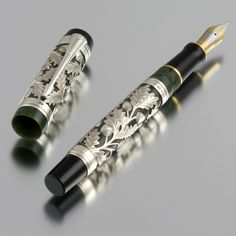 two fountain pens sitting next to each other on top of a gray surface with gold trimming