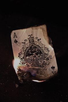 an ace playing card sitting on top of a table next to a lit matchstick