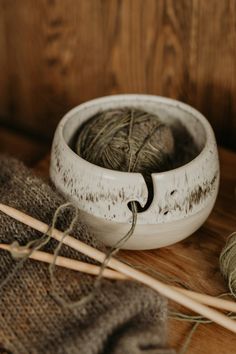 a white bowl sitting on top of a wooden table next to yarn and knitting needles