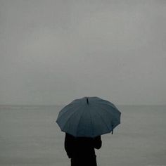 a person standing on the beach with an umbrella over their head, looking out at the ocean