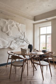 a dining room table with four chairs and a vase on top of it in front of a large painting