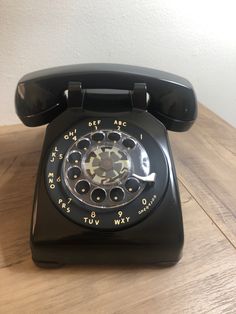 an old black rotary telephone on a wooden table