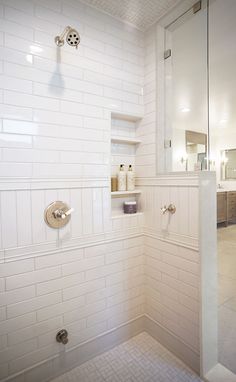 a white tiled bathroom with glass shower doors and shelves on the wall, along with toiletries