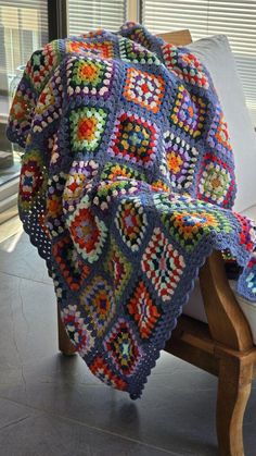 a crocheted blanket sitting on top of a wooden chair next to a window