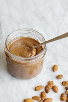 almonds and peanut butter in a jar on a marble counter top with a spoon