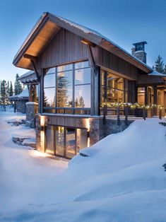 a house in the snow with lights on it's windows and some trees around