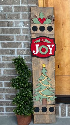 a wooden sign that says joy with a christmas tree on it next to a potted plant