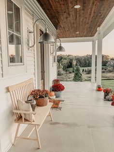 a wooden bench sitting on top of a porch next to a white house with red flowers