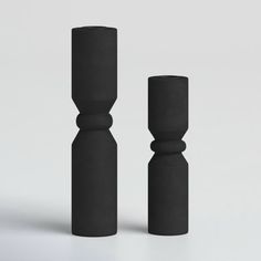 two black candlesticks sitting next to each other on a white surface with one candle in the middle