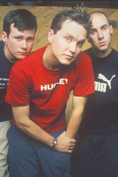 three young men sitting next to each other in front of a wooden floor and wall