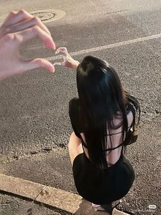 a woman is sitting on the curb with her hand reaching for something in front of her