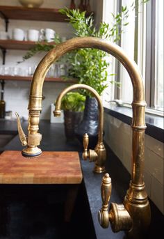 a kitchen sink with brass faucets in front of a window