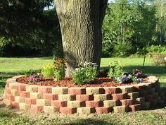 a brick wall around a tree in a yard with flowers growing on the ground below