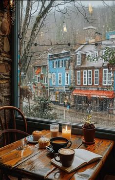 two cups of coffee sit on a wooden table in front of a window with a view of the city outside