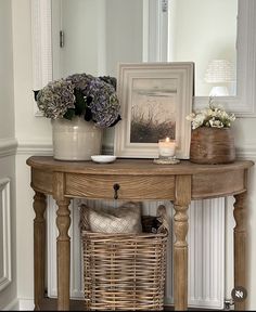 a wooden table topped with a basket filled with flowers next to a mirror and framed photograph