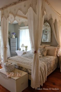 a white bed sitting inside of a bedroom next to a dresser and window covered in curtains