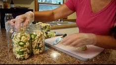 a woman in pink shirt preparing food on top of a kitchen counter next to glass jars