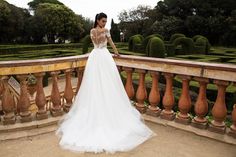 a woman in a wedding dress is standing on a balcony overlooking an ornamental garden area