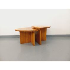 two wooden tables sitting next to each other on top of a cement floor in front of a white wall