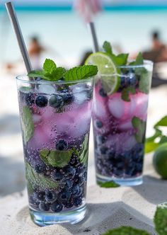 two glasses filled with blueberries and limeade on the beach