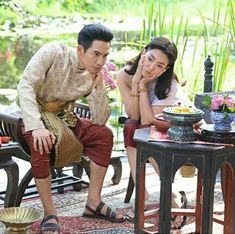 a man and woman sitting on wooden benches next to each other in front of a pond