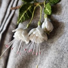 two white flowers are hanging from a green leafy plant on a gray shirt with pink and white pins