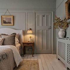 a white bed sitting in a bedroom next to a dresser and lamp on top of a wooden floor