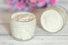 a jar filled with cream sitting on top of a wooden table next to pink flowers