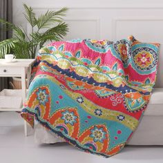 a colorful blanket sitting on top of a bed next to a potted palm tree