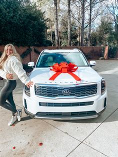 a woman standing next to a white car with a red bow on it