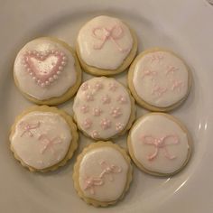 six decorated cookies on a white plate with pink bows and heart shaped frosting in the middle