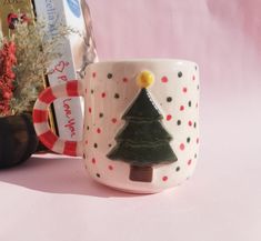 a coffee cup with a christmas tree on it next to some books and a plant