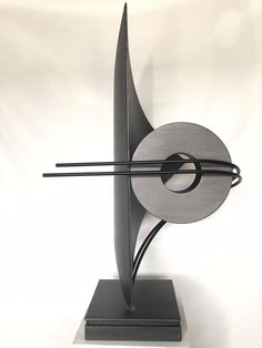 a metal sculpture on a white surface with a black object in the center and two sticks sticking out of it