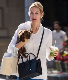 a woman holding a small dog in her right hand while walking down the street with two bags